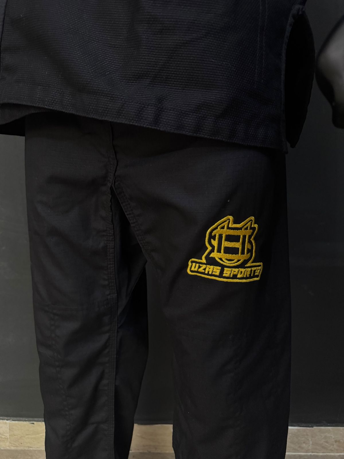 Black karate uniform pants with a gold embroidered logo
