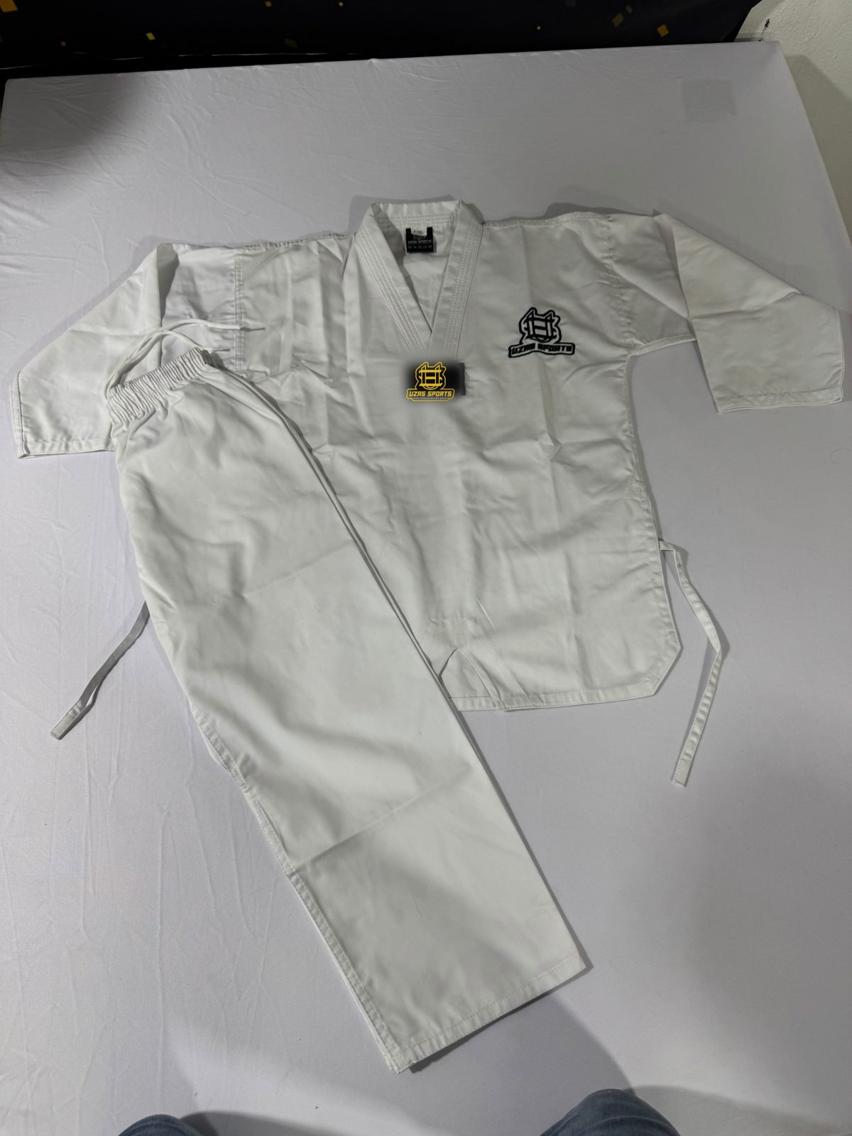 White taekwondo uniform with jacket, pants and belt laid flat