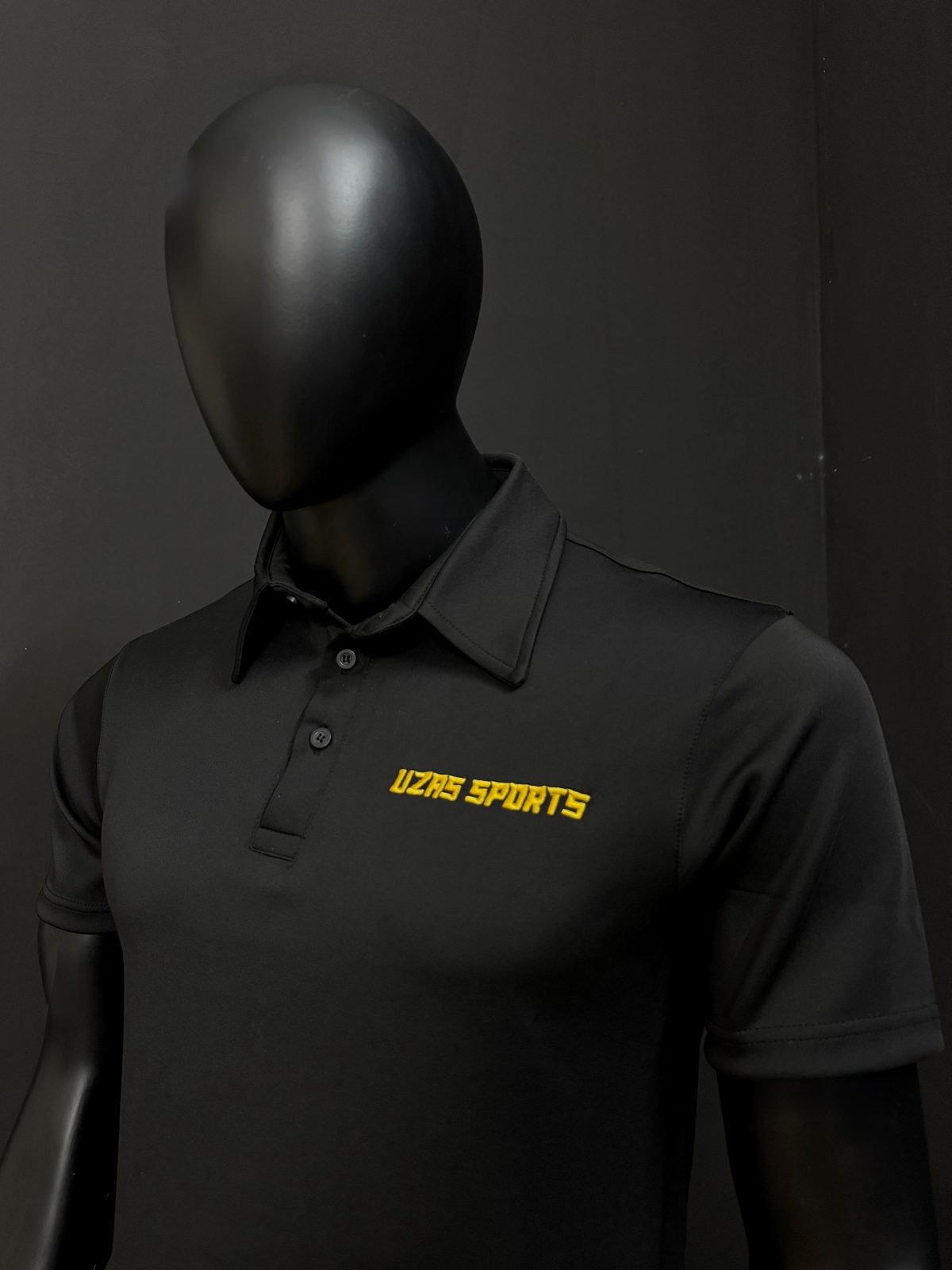 Black polo shirt with an embroidered UZAS Sports chest logo